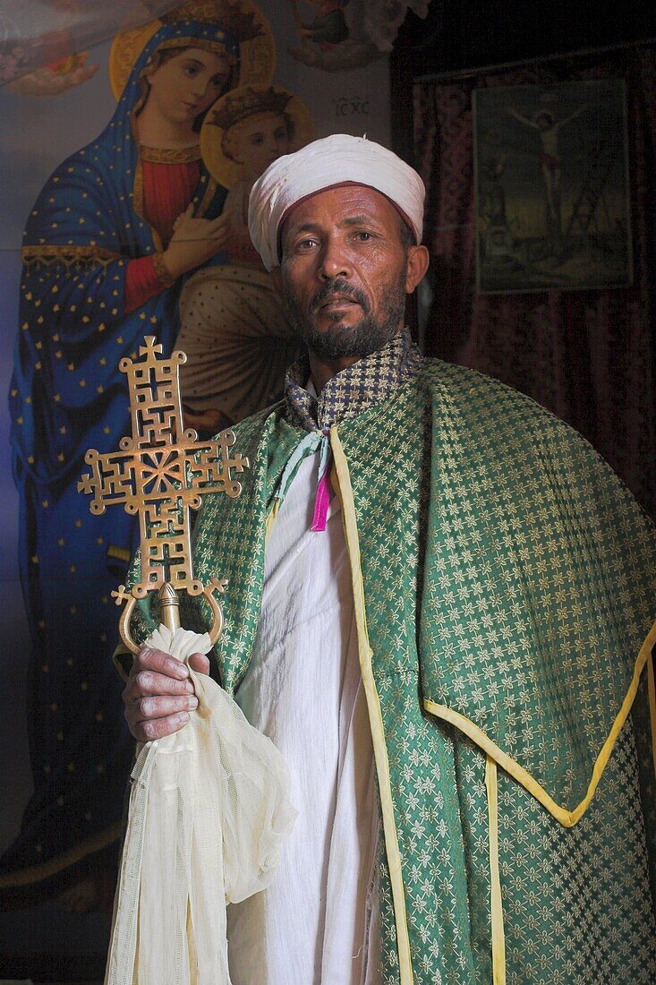 Priest with cross, Bet Meskel, an excavated chapel in the northern wall of the courtyard of Bet Maryam, Lalibela, Ethiopia, Africa