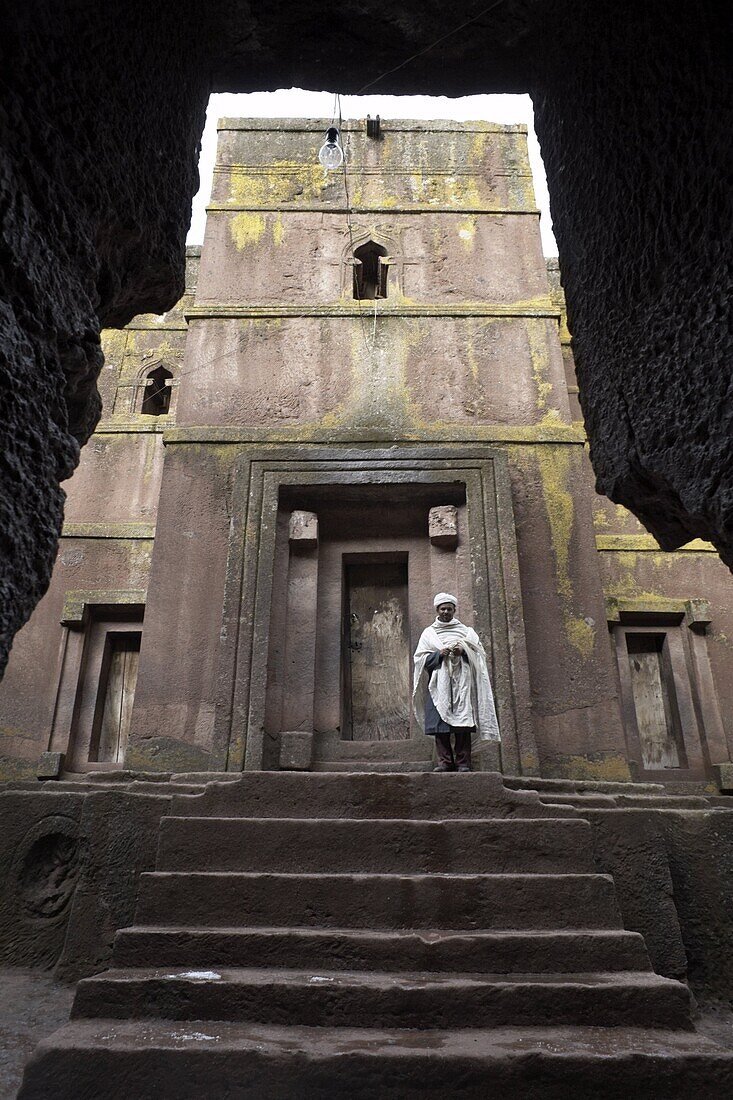 A priest stands at the entrance to the rock-hewn church of Bet Giyorgis (St. George), in Lalibela, UNESCO World Heritage Site, Ethiopia, Africa