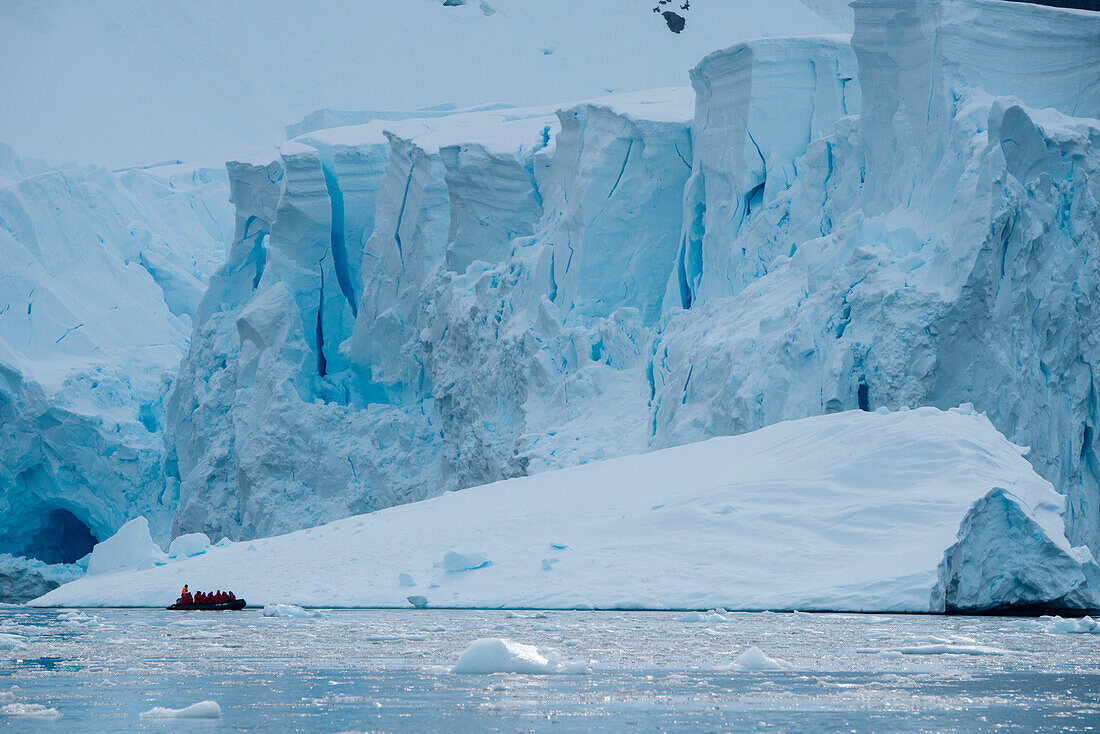 Passengers in a Zodiac dinghy of expedition cruise ship MS Hanseatic (Hapag-Lloyd Cruises) are dwarfed by an iceberg and the edge of the glacier, Paradise Bay (Paradise Harbor), Danco Coast, Graham Land, Antarctica
