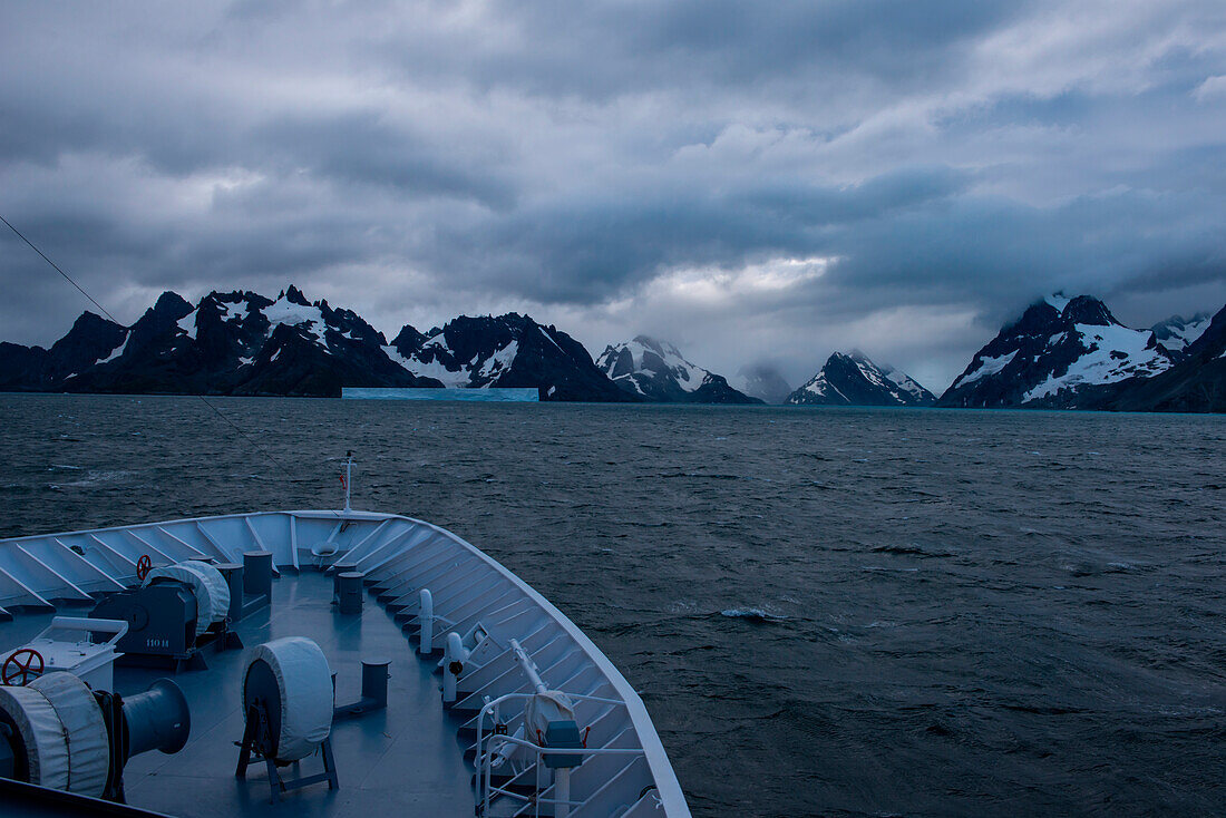 Bow of expedition cruise ship MS Hanseatic (Hapag-Lloyd Cruises) with iceberg and mountains in distance, Drygalsky Fjord, South Georgia Island, Antarctica