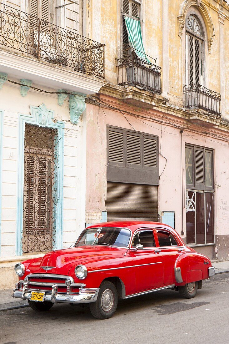 Restrored red American car pakred outside faded Colonial buildings, Havana, Cuba, West Indies, Central America