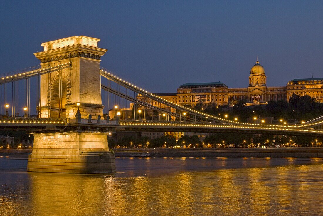 The Chain Bridge (Szechenyi Lanchid), over the River Danube, illuminated at sunset with the Hungarian National Gallery also lit, behind, Budapest, Hungary, Europe