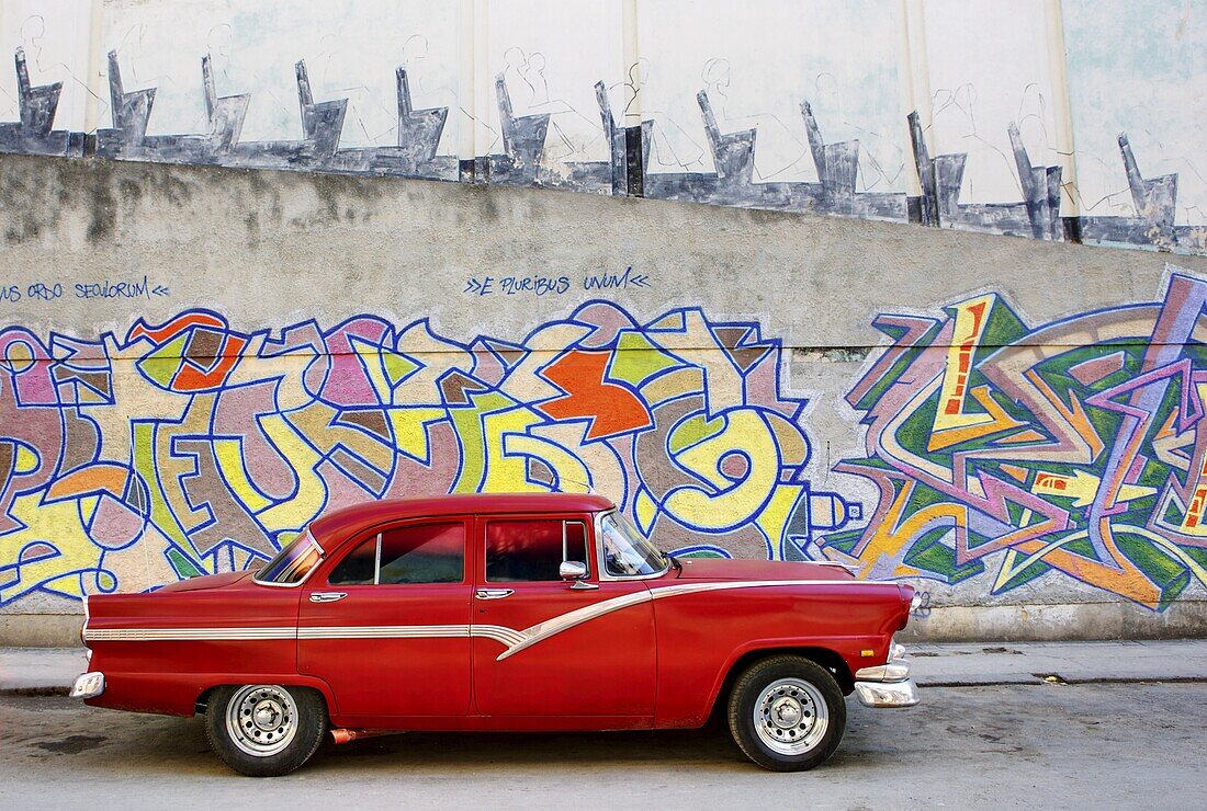 Classic red American car parked in front of grafitti covered wall, Havana, Cuba, West Indies, Central America