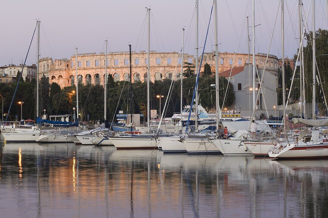 Yachts in the harbour, with the 1st century Roman amphitheatre beyond in evening light, Pula, Istria coast, Croatia, Adriatic, Europe
