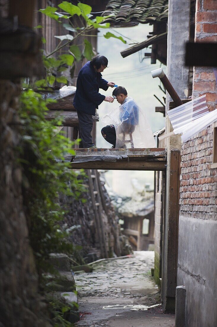 An outdoor barber cutting a boy's hair in Langde village, Guizhou Province, China, Asia