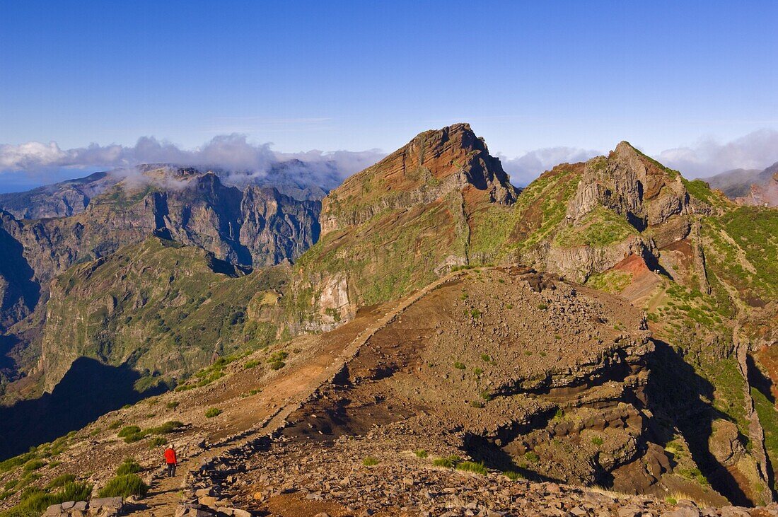 Hiker in red jacket walking down new footpath across the volcanic landscape towards Madeira's third highest peak, Pico do Arieiro, Madeira, Portugal, Europe