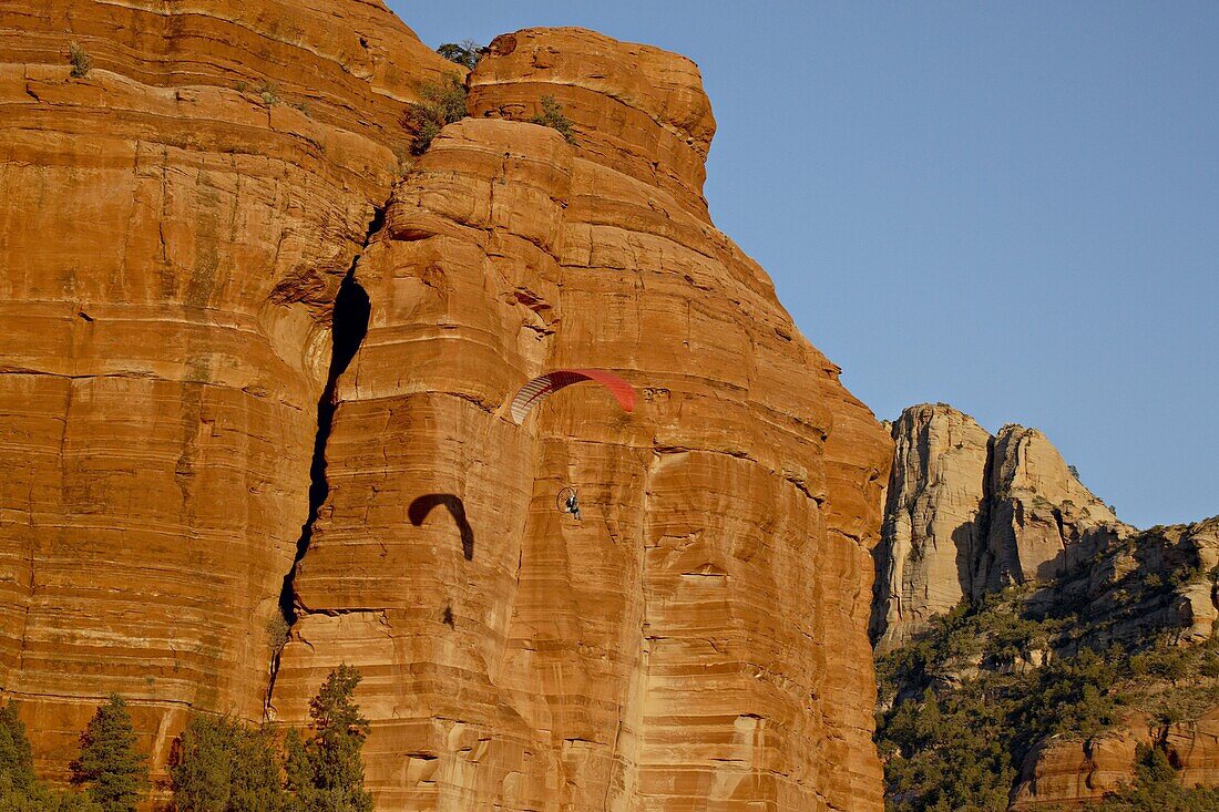 A paraglider flies past a red rock formation, Coconino National Forest, Arizona, United States of America, North America