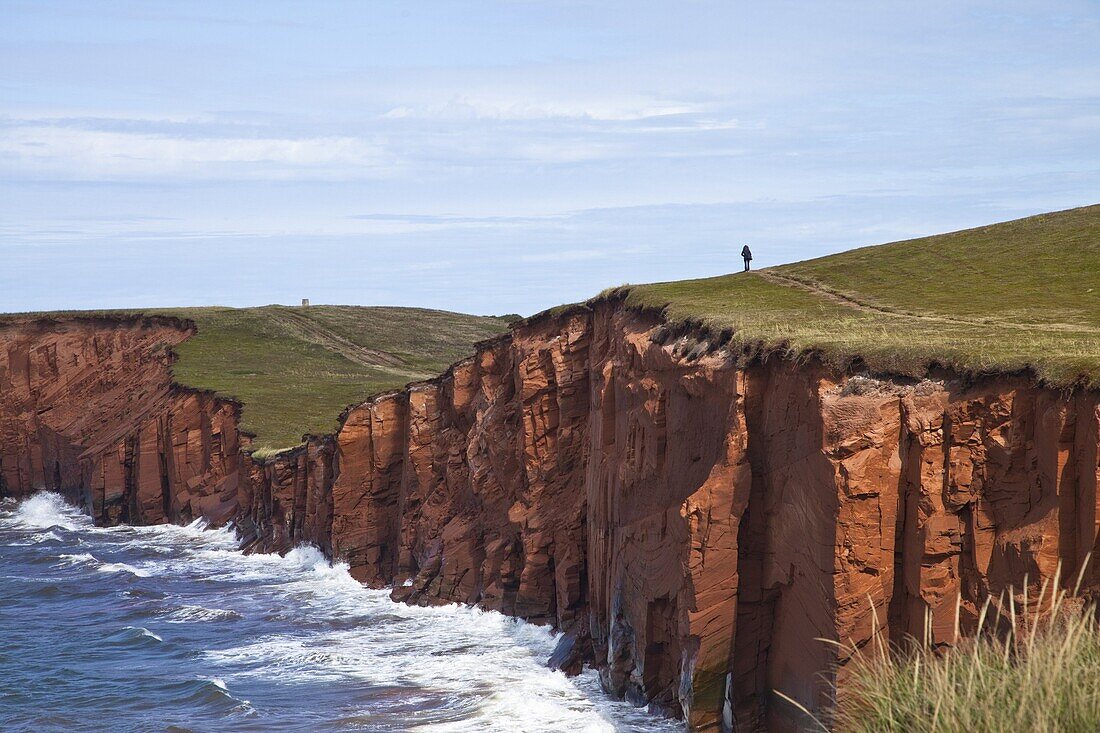 Person walking on red sandstone cliff on Cap-aux-Meules Island in the Iles de la Madeleine (Magdalen Islands), Quebec, Canada, North America
