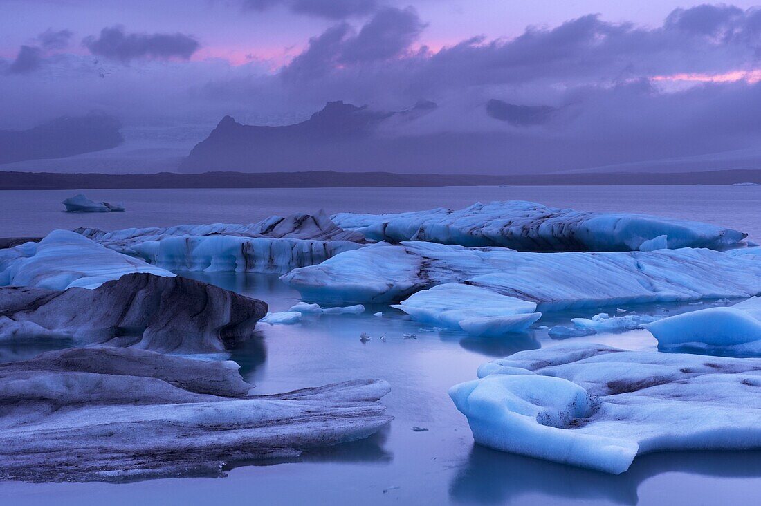Icebergs in Jokulsarlon glacial lagoon, at dusk, Oraefajokull (Vatnajokull) glacier in the distance, East Iceland, Iceland, Polar Regions