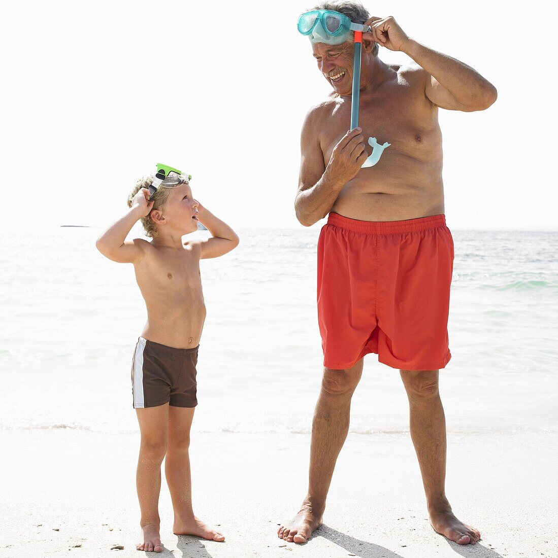 Grandfather and grandson (6-8) on beach with snorkelling masks