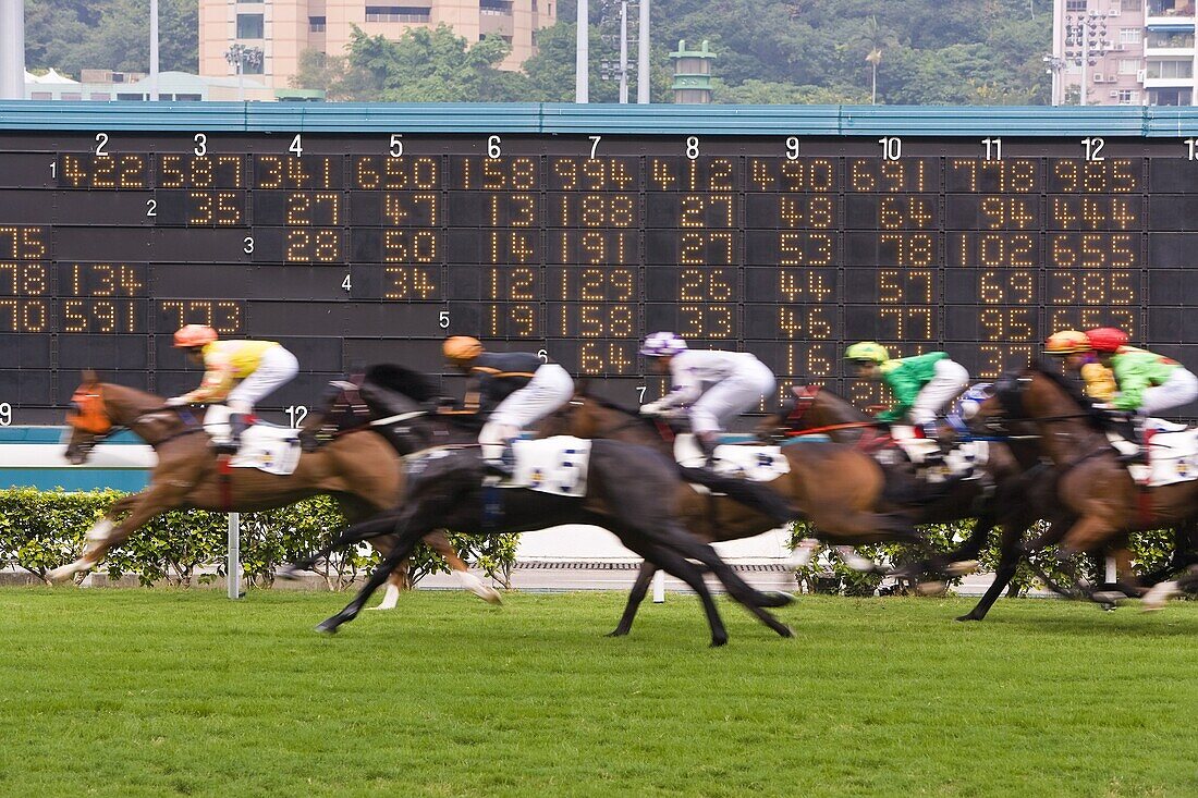 Horses race past large scoreboard during race at Happy Valley racecourse, Hong Kong, China, Asia