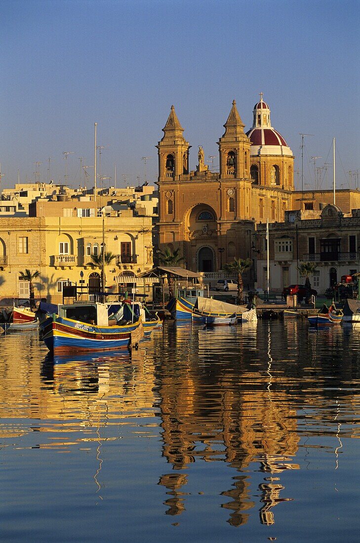 Harbour with Luzzu fishing boats and Marsaxlokk Parish Church at sunrise, Marsaxlokk, Malta, Mediterranean, Europe
