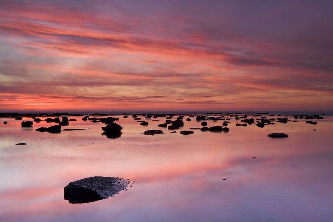 Boulders and reflections in the sea at sunrise, Saltwick Bay, Yorkshire, England, United Kingdom, Europe