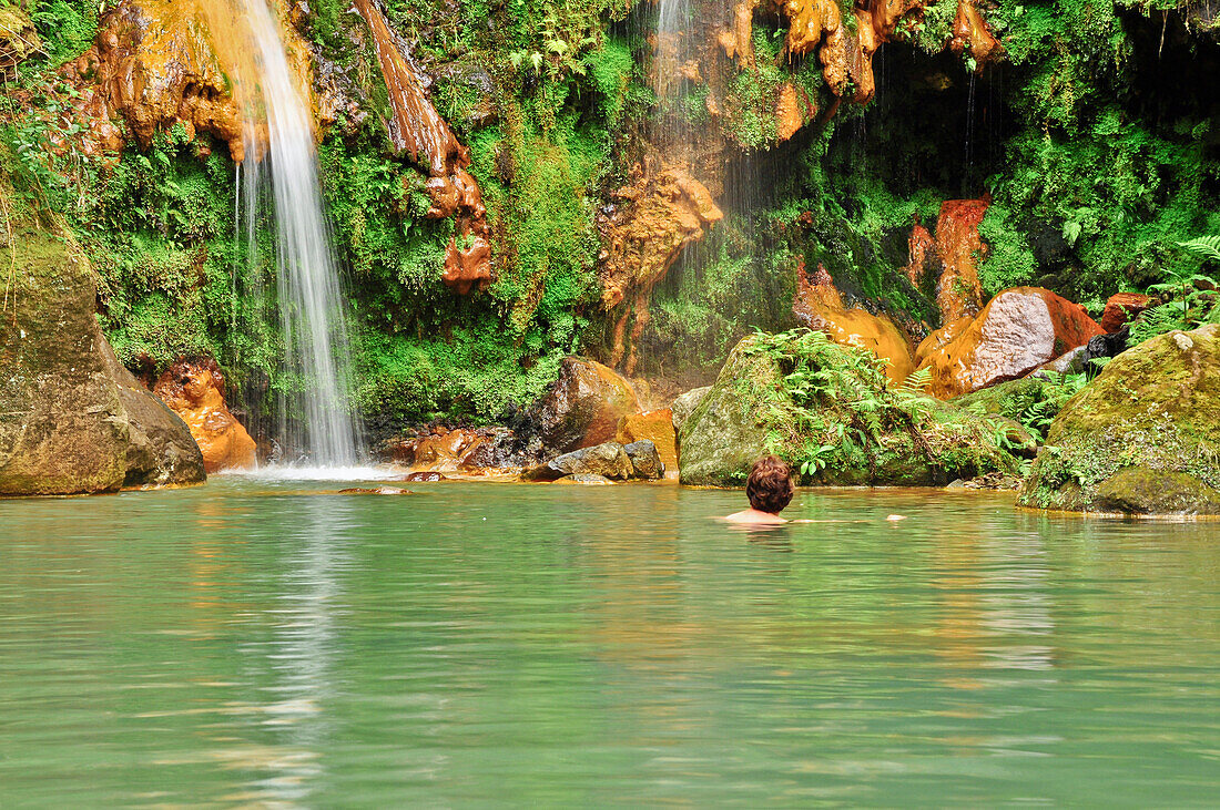 Frau schwimmt und badet im warmen Wasser der heißen Quelle Caldeira Velha unter einem Wasserfall, Vulkan Volcao do Fogo, Ribeira Grande, Insel Sao Miguel, Azoren, Portugal, Europa, Atlantik