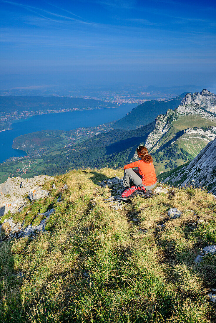 Woman hiking sitting on grassy ledge and looking towards Lac d'Annecy, Tournette, La Tournette, Haute-Savoie, France