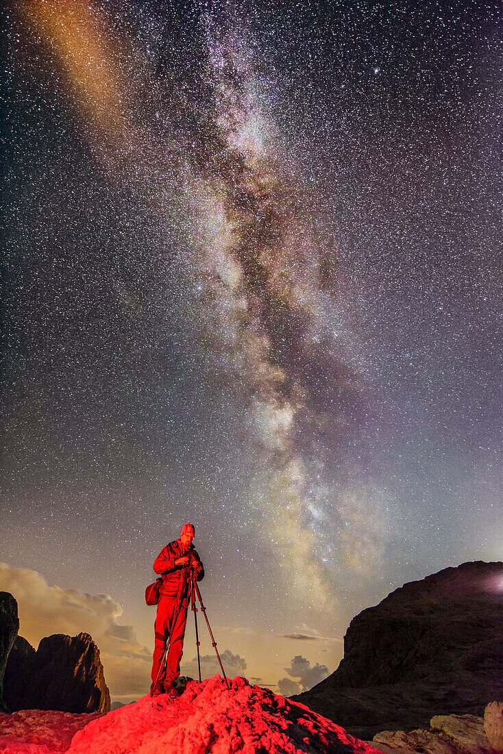 Photographer standing on rock beneath stary sky with milky way, Pala range, Dolomites, UNESCO World Heritage Dolomites, Trentino, Italy