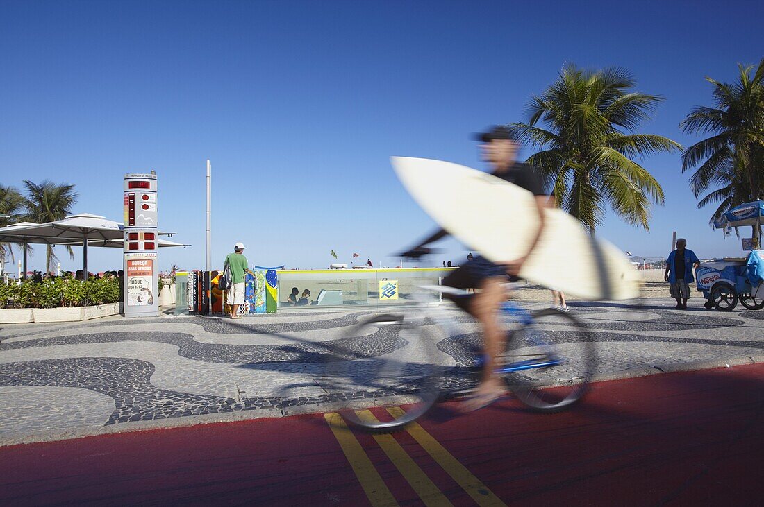 Man with surfboard cycling along Avenida Atlantica, Copacabana, Rio de Janeiro, Brazil, South America