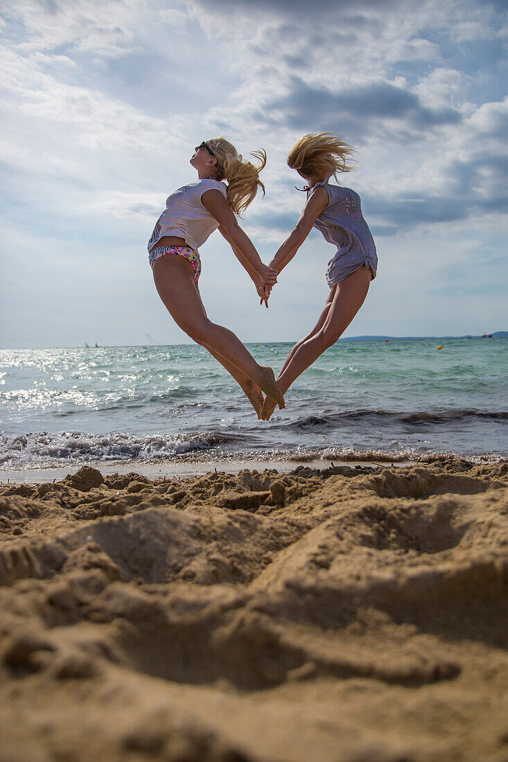 Two young women jumping in the air from the beach in the shape of a heart, 'S Arenal, Palma, Mallorca, Balearic Islands, Spain