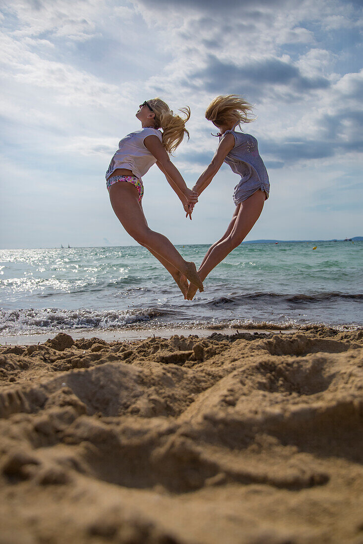 Zwei junge Frauen springen vom Strand in die Luft und formen dabei ein Herz, 'S Arenal, Palma, Mallorca, Balearic Islands, Spain