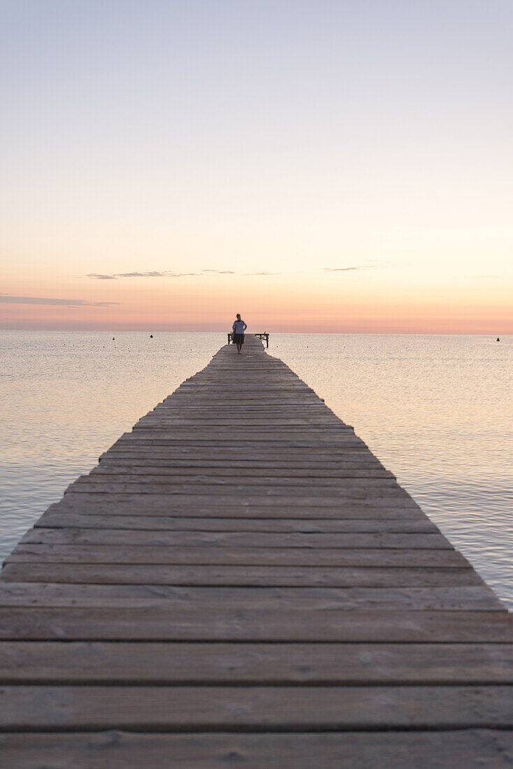 Frau geht auf einem langen Steg in der Morgenstimmung. Strand Playa de Muro, Alcudia, Mallorca, Balearen, Spanien
