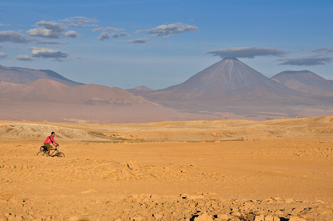 Young man rides a bicycle through desert, volcano Licancabur, Valle de la Luna, Valley of the moon, Atacama desert, National Reserve, Reserva Nacional Los Flamencos, Region de Antofagasta, Andes, Chile, South America