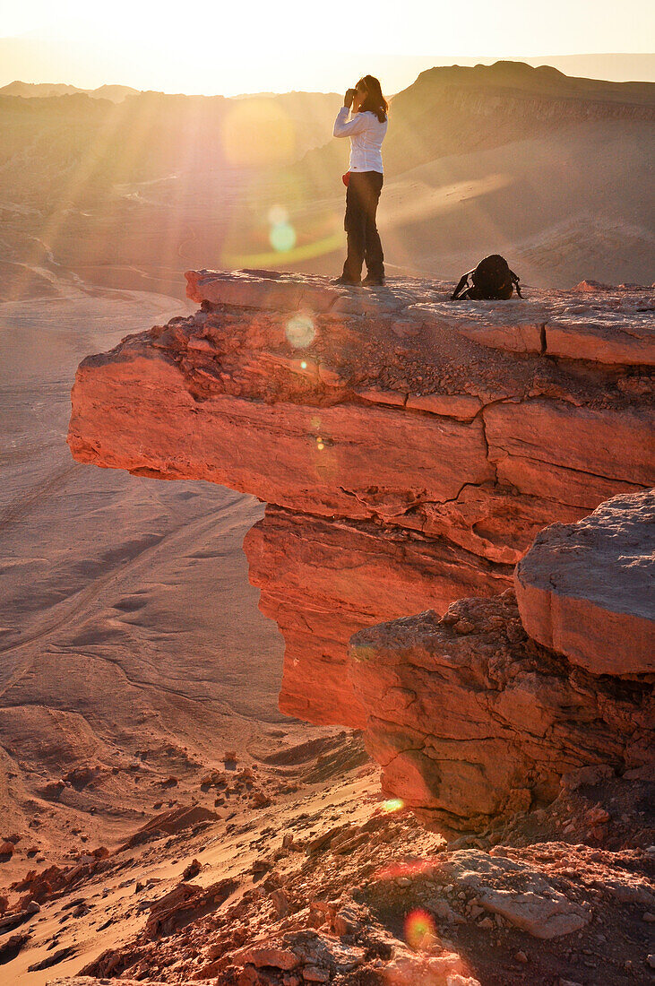 'Junge Frau steht auf Felsen und genießt Aussicht bei Sonnenuntergang, Valle de la Luna, Tal des Mondes, Atacama Wüste, Reserva Nacional Los Flamencos, Region de Antofagasta, Anden, Chile, Südamerika, Amerika;'