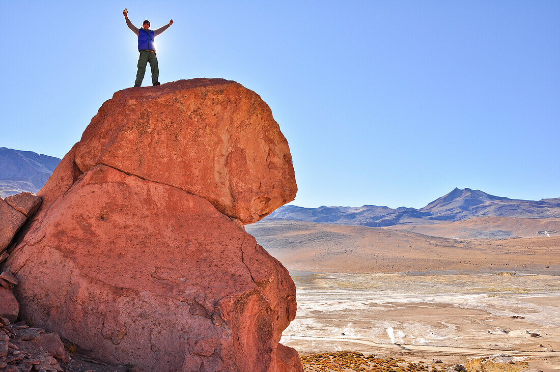 'Junger Mann, Bergsteiger steht auf Felsen und genießt Aussicht auf Geysire und Vulkane, Geysirfeld El Tatio, Atacama Wüste, Reserva Nacional Los Flamencos, Region de Antofagasta, Chile, Südamerika, Amerika;'