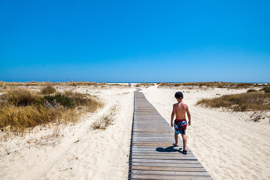 Boy on a boardwalk, walking to the beach, Armona island, Olhao, Algarve, Portugal