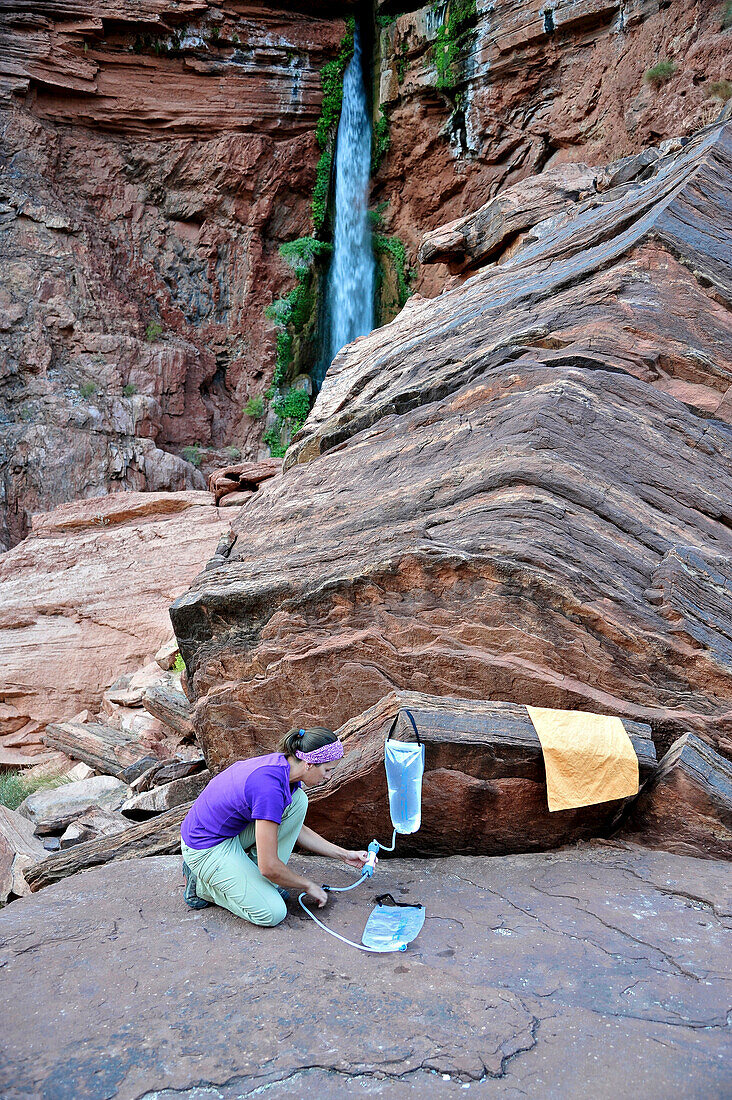 Female hiker filters water on a cliff-pinched patio near Deer Creek Falls in the Grand Canyon outside of Fredonia, Arizona November 2011.  The 21.4-mile loop starts at the Bill Hall trailhead on the North Rim and descends 2000-feet in 2.5-miles through Co