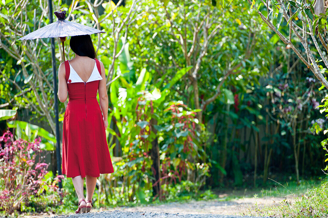 Beautiful woman in red dress walking through a Thai garden