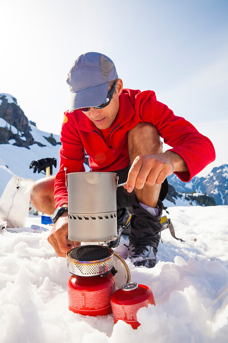 A climber uses a camping stove to make his dinner while camping in the mountains.