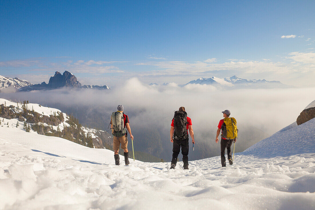 Three backpackers cross a snowfield after a trip into the mountains of British Columbia, Canada.