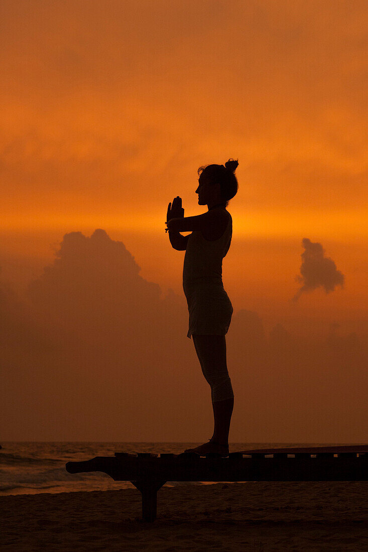 Mädchen macht Yoga bei Sonnenuntergang am Strand von Sri Lanka