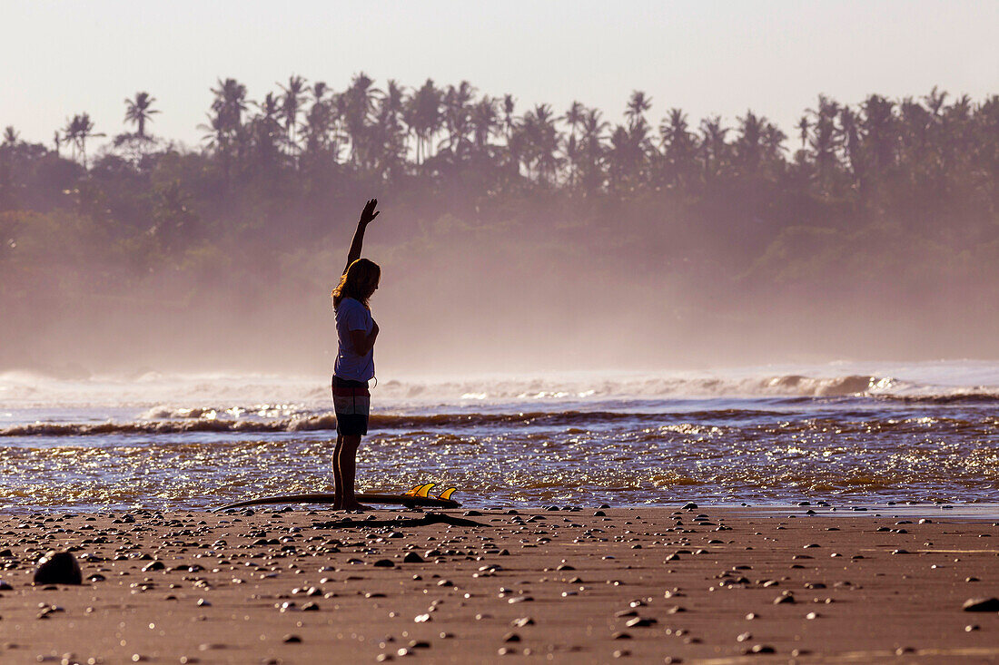 Young man stretching on the beach before surfing