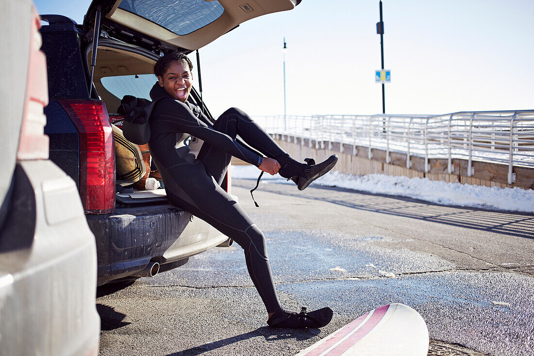 Black teenage girl putting on wetsuit