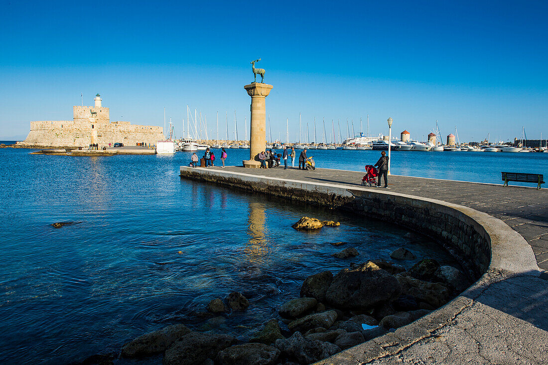 The old Agios Nikolaos fortress and lighthouse in Mandraki Harbour with deer statue in foreground, Rhodes Town, Rhodes, Dodecanese Islands, Greek Islands, Greece, Europe