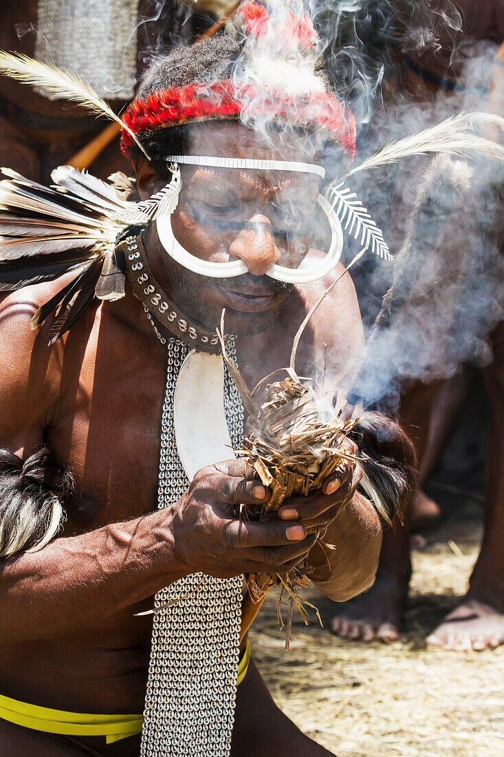 Dani men wearing an elaborate headdress of bird of paradise or cassowary feathers lighting a fire, Obia Village, Baliem Valley, Central Highlands of Western New Guinea, Papua, Indonesia