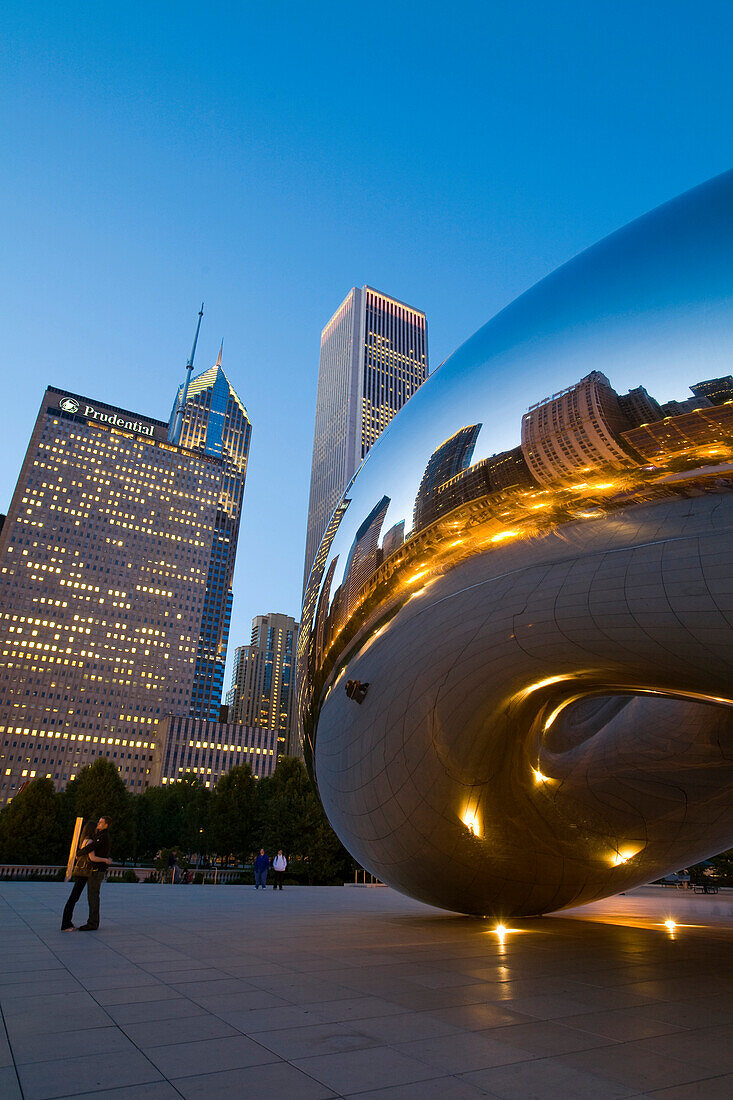 Illinois Chicago Bean Sculpture In Millennium Park At Dusk, City And Buildings Reflected In Modern Metal Public Art, Couple Hug In Plaza