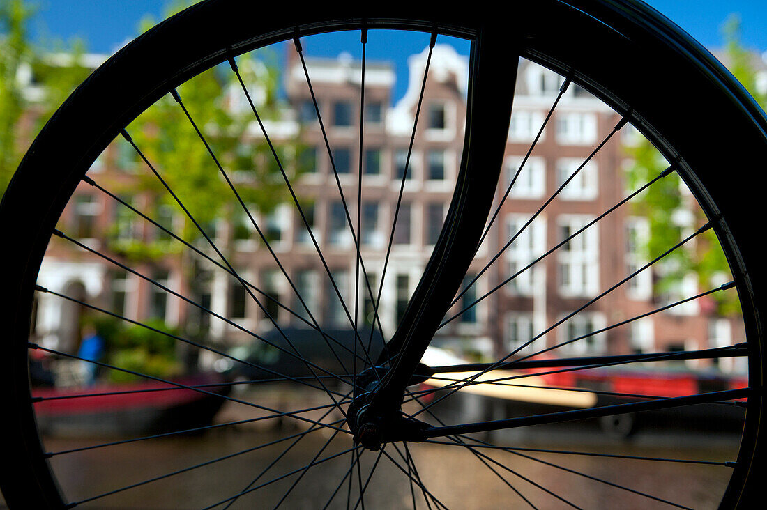 Silhouette of bicycle wheel in front of canal and traditional gabled houses, Amsterdam, Holland