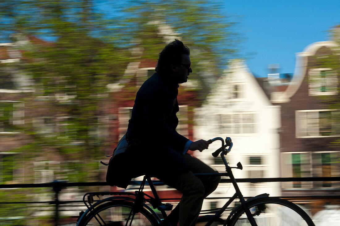 Silhouette of cyclist going past canal and gabled houses, Amsterdam, Holland