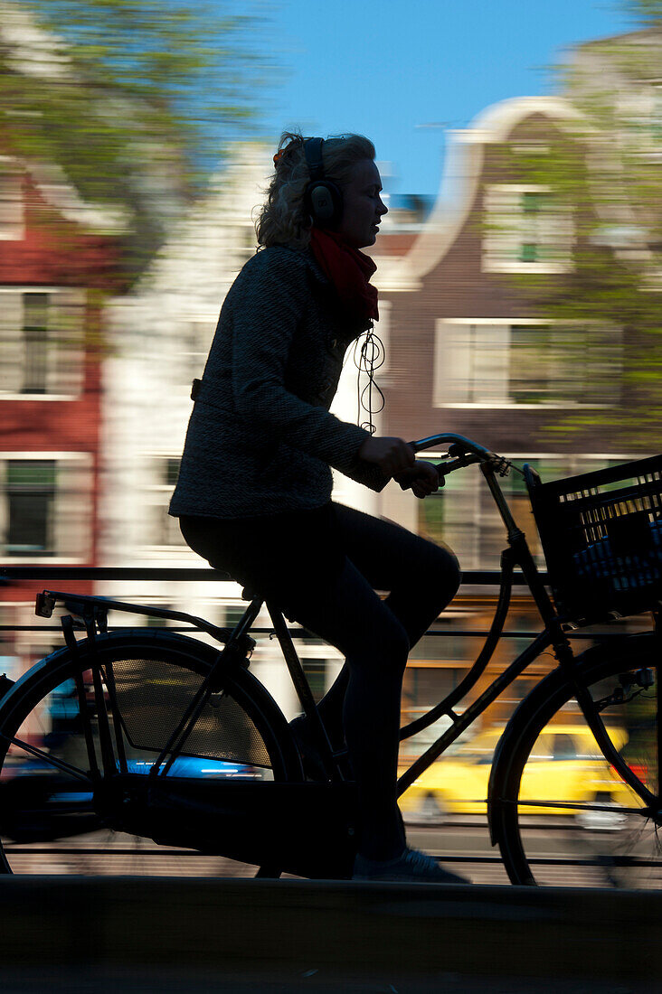 Silhouette of cyclist going past canal and gabled houses, Amsterdam, Holland