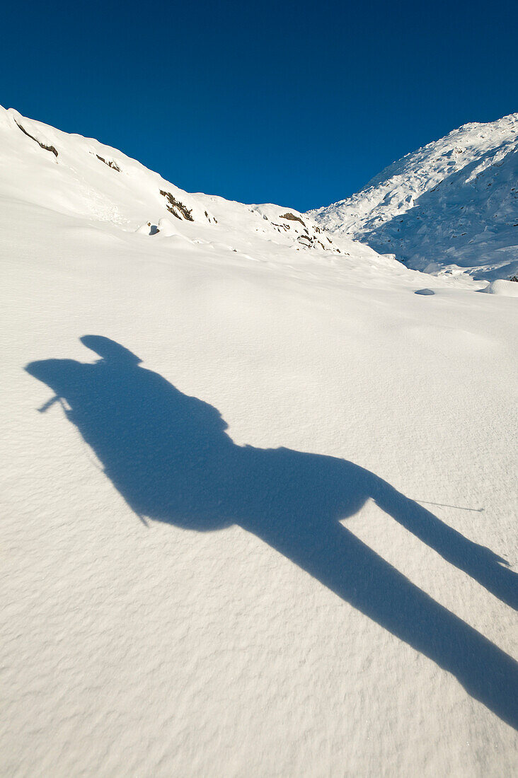 Shadow of walker with rucksack going up snowy slopes of Beinn Respiol, Ardnamurchan peninsula, Highlands, Scotland