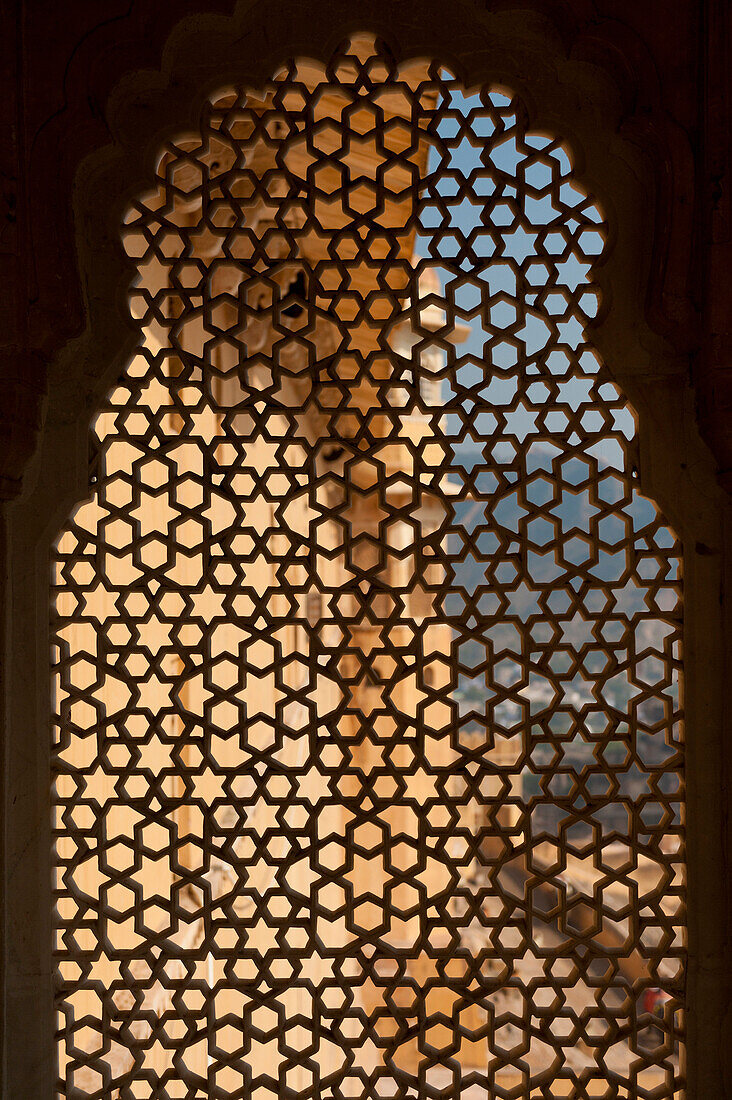 Looking through stone lattice window to the walls of Amber Fort, Amer, Jaipur, India