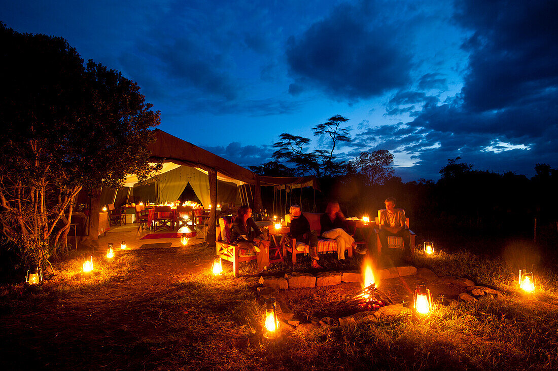 People sitting around fire at dusk in front of dining tent, Ol Pejeta Camp, Ol Pejeta Conservancy, Kenya
