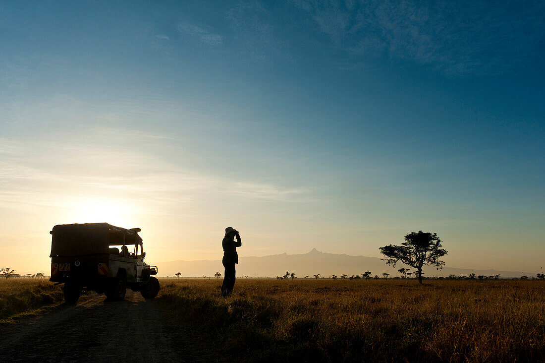 Silhouette of woman looking through binoculars in front of Mt Kenya at dawn, Ol Pejeta Conservancy, Kenya