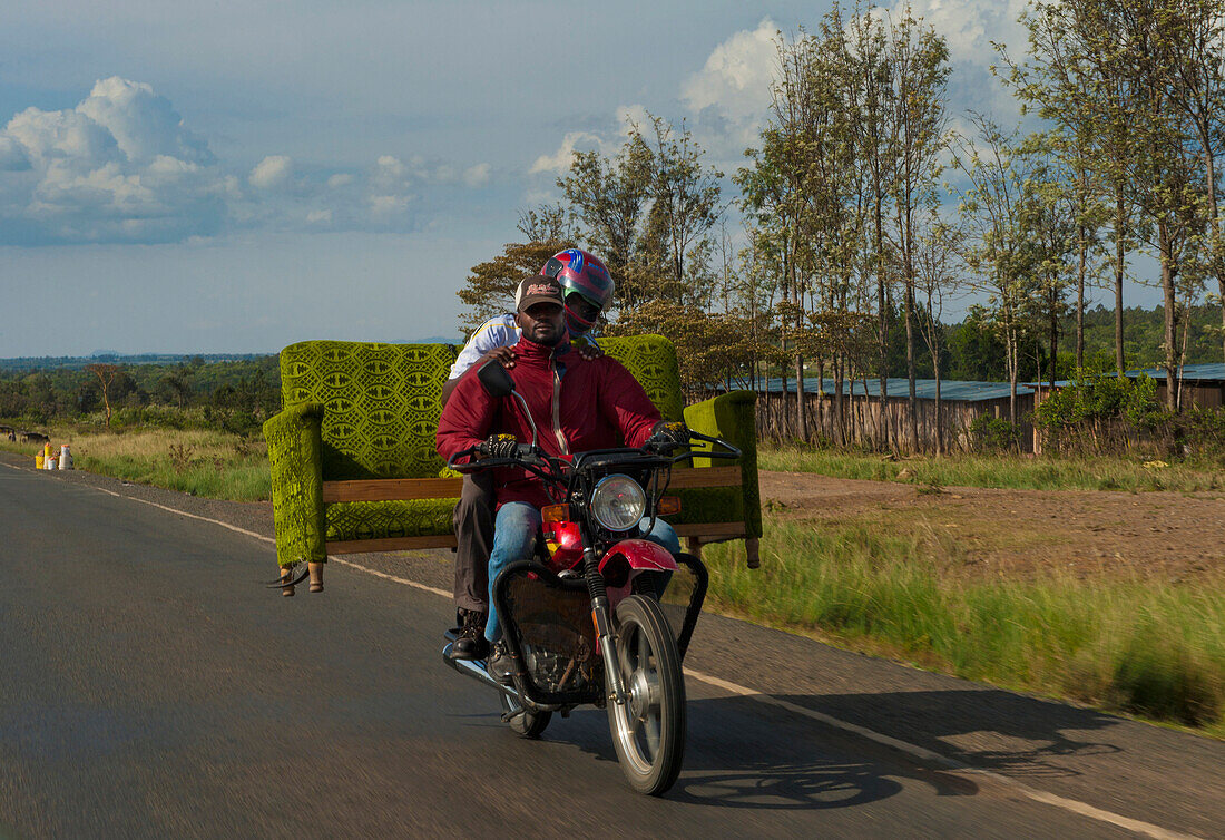 Two men on motorbike carrying sofa on back on road, near Nanyuki, Kenya