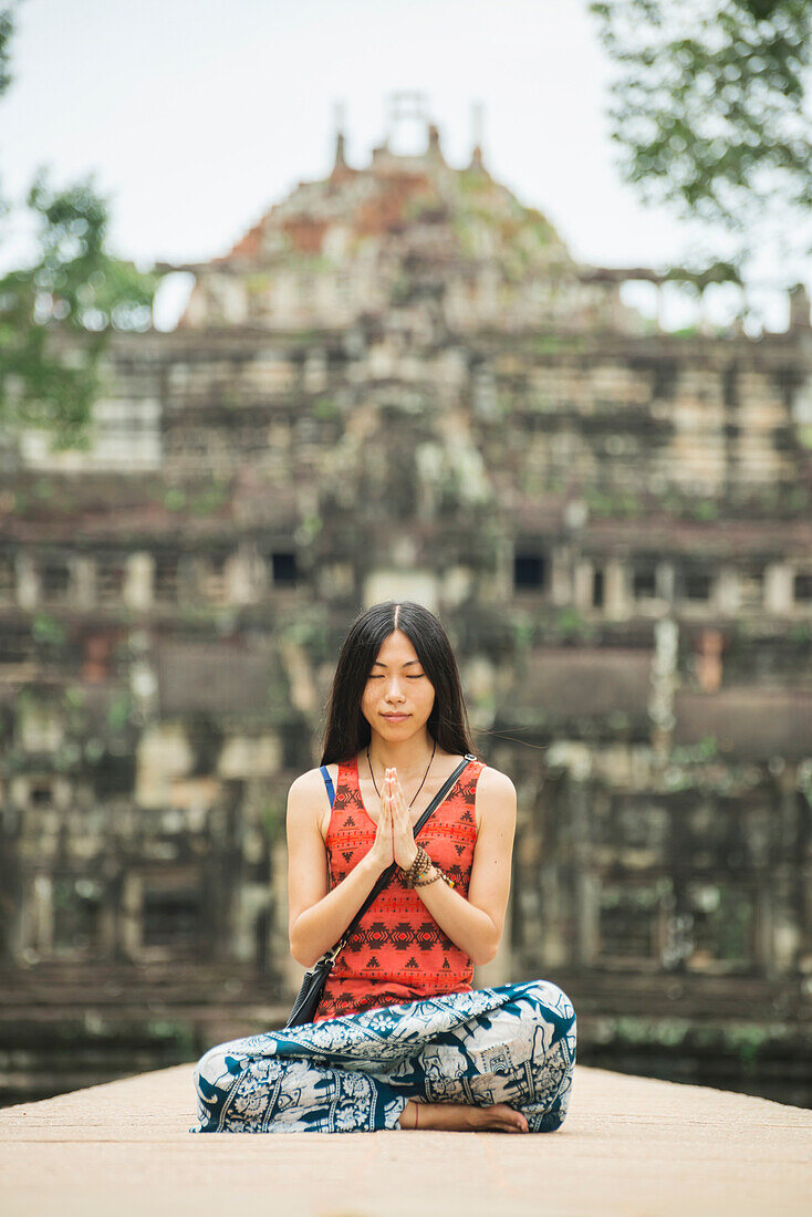 A young woman in meditation on Baphuon Temple is just next to Bayon Wat, built in Eleventh Century by Udayadityavarman II dedicated to the Hindu God Shiva, Angkor, Siem Reap, Cambodia