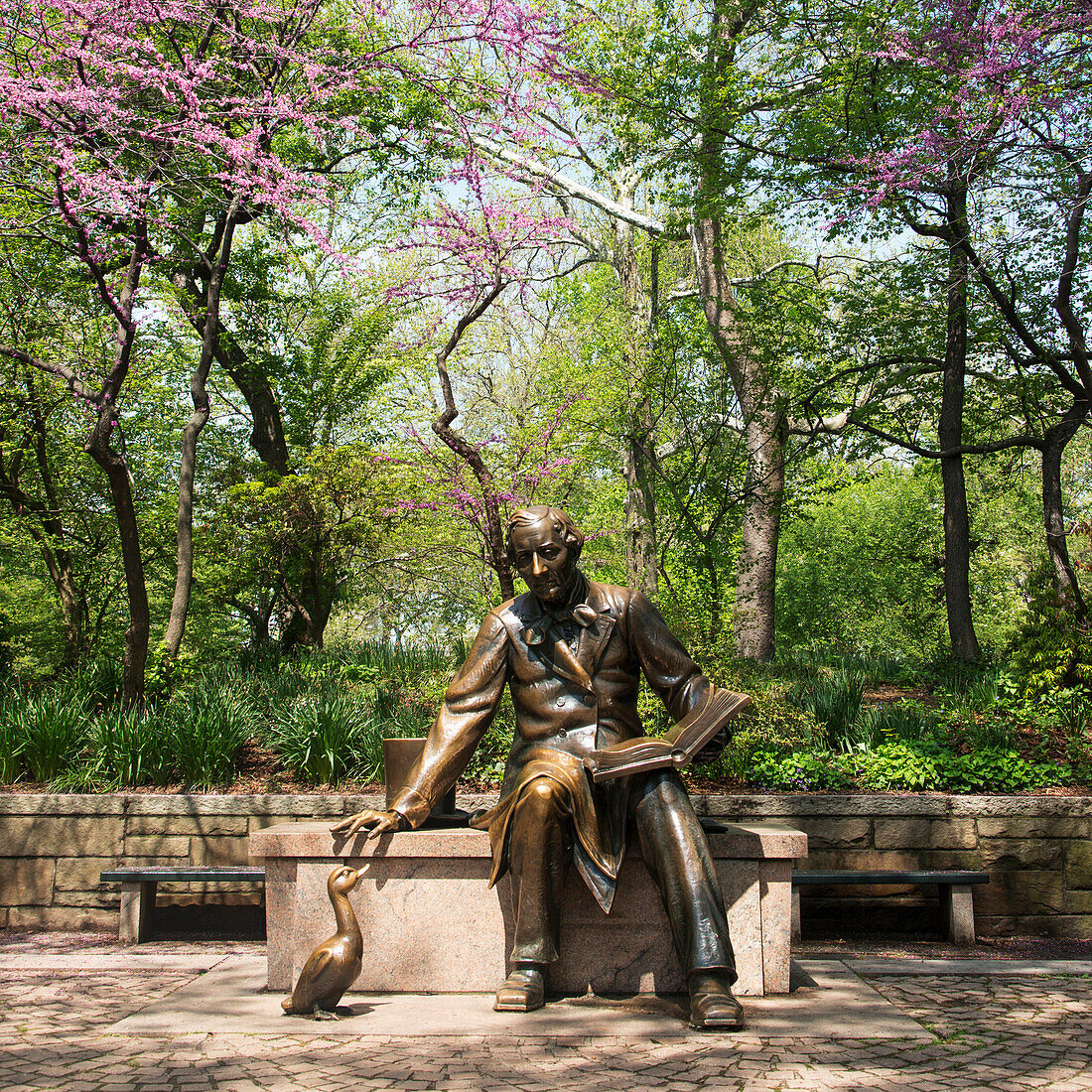 'Statue of a man sitting and reading on a bench in an urban park; New York City, New York, United States of America'