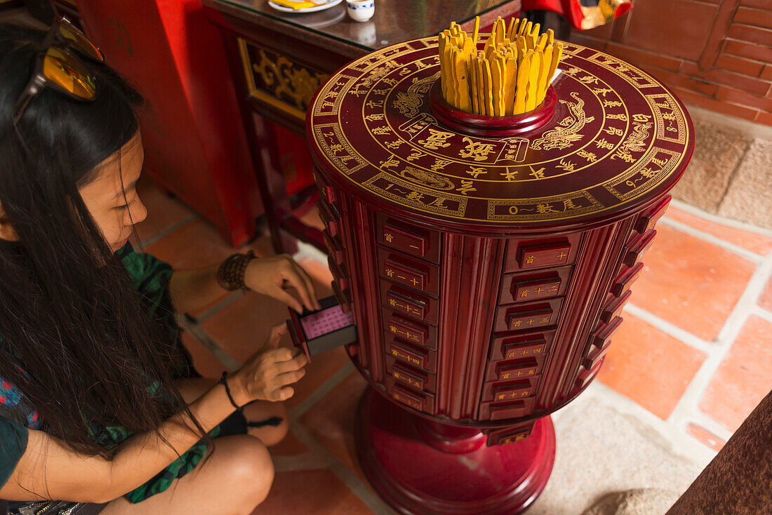 'Chinese young woman trying the traditional roll of fortune in a Buddhist temple; Shanzidou, Kinmen Island, Taiwan'