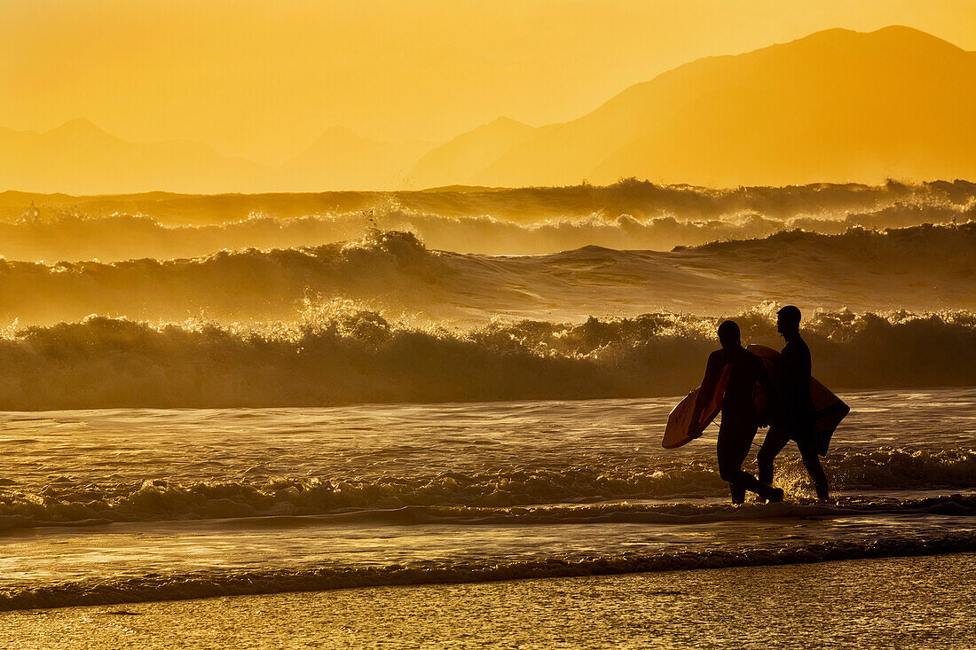 Body surfers walk in the water on the coast of Kodiak Island during late afternoon, Pasagshak State Park, Kodiak Island, Alaska